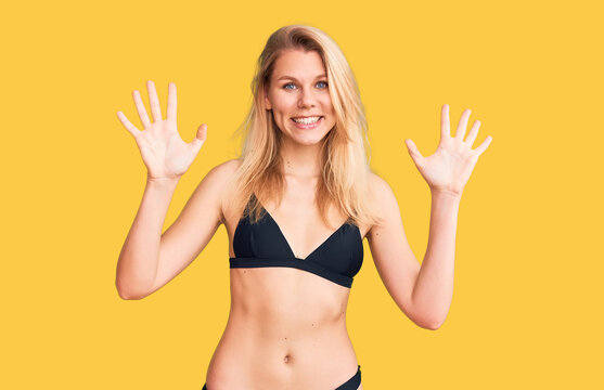 Young beautiful blonde woman wearing bikini showing and pointing up with fingers number ten while smiling confident and happy.