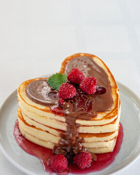 Homemade heart shaped pancakes stack with chocolate and raspberries