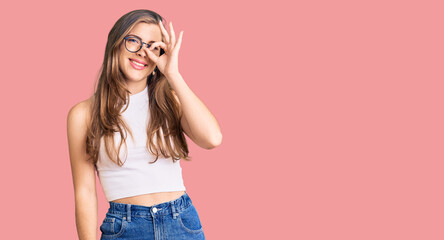 Beautiful caucasian young woman wearing casual clothes and glasses doing ok gesture with hand smiling, eye looking through fingers with happy face.