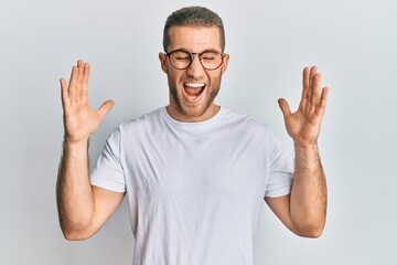 Fototapeta premium Young caucasian man wearing casual clothes and glasses celebrating mad and crazy for success with arms raised and closed eyes screaming excited. winner concept
