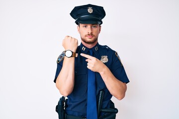 Young caucasian man wearing police uniform in hurry pointing to watch time, impatience, looking at the camera with relaxed expression
