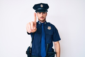 Young caucasian man wearing police uniform pointing with finger up and angry expression, showing no...