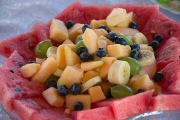Plate with raw sliced fruits on a table - blueberries, melon, watermelon, banana, grapes, healthy snacks, party concept, appetizers for celebration, nutritious food