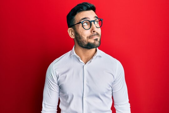Young hispanic businessman wearing shirt and glasses smiling looking to the side and staring away thinking.