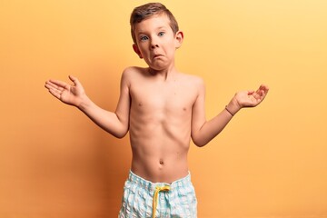 Cute blond kid wearing swimwear clueless and confused with open arms, no idea and doubtful face.