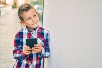 Adorable caucasian boy smiling happy using smartphone at the city.