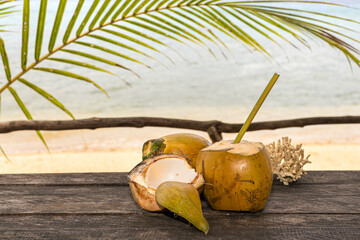 open coconut with a straw on a wooden bench on the beach in Vanuatu