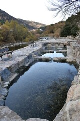 Stone thermal water pools and wooden benches next to the Cidacos river. Hot springs in the village of Arnedillo. Winter day without people.