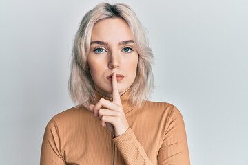 Naklejka premium Young blonde girl wearing casual clothes asking to be quiet with finger on lips. silence and secret concept.