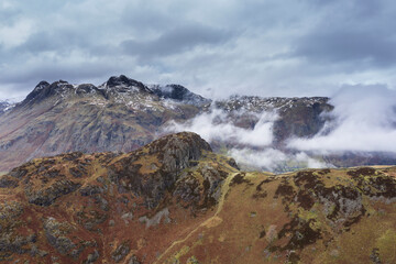 Stunning flying drone landscape image of Langdale pikes and valley in Winter with dramatic low level clouds and mist swirling around