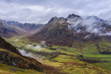 Fototapeta premium Stunning flying drone landscape image of Langdale pikes and valley in Winter with dramatic low level clouds and mist swirling around