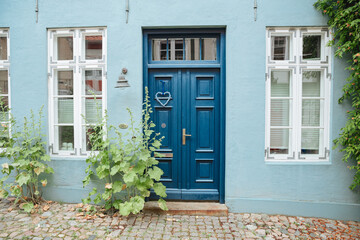Blue house wall with a blue wooden door and a green plant at the entrance. House in Germany