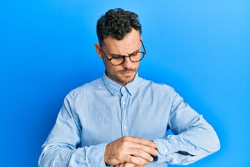 Young hispanic man wearing casual clothes and glasses checking the time on wrist watch, relaxed and...