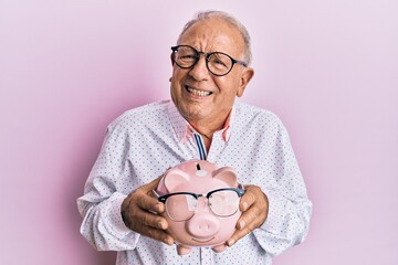 Senior caucasian man holding piggy bank with glasses clueless and confused expression. doubt...
