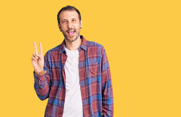 Young handsome man wearing casual clothes smiling with happy face winking at the camera doing victory sign with fingers. number two.