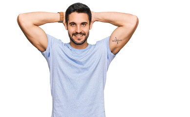 Young hispanic man wearing casual clothes relaxing and stretching, arms and hands behind head and neck smiling happy