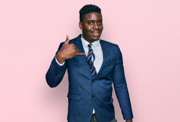 Handsome business black man wearing business suit and tie smiling doing phone gesture with hand and fingers like talking on the telephone. communicating concepts.