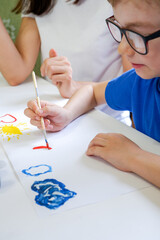 Cute little child draws at the table with paints with his mother close-up. Game room.