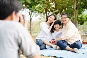 Happy Asian family have come picnic in park together for summer holidays. Boy enjoy travel with their mother and grandma in the park Beautiful nature. Concept Health care insurance