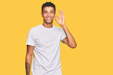 Young handsome african american man wearing casual white tshirt smiling positive doing ok sign with hand and fingers. successful expression.