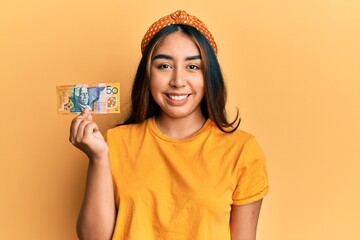 Young latin woman holding 50 australian dollar banknote looking positive and happy standing and smiling with a confident smile showing teeth