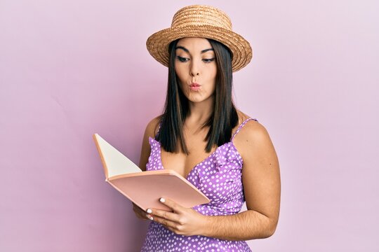 Young brunette woman reading book making fish face with mouth and squinting eyes, crazy and comical.