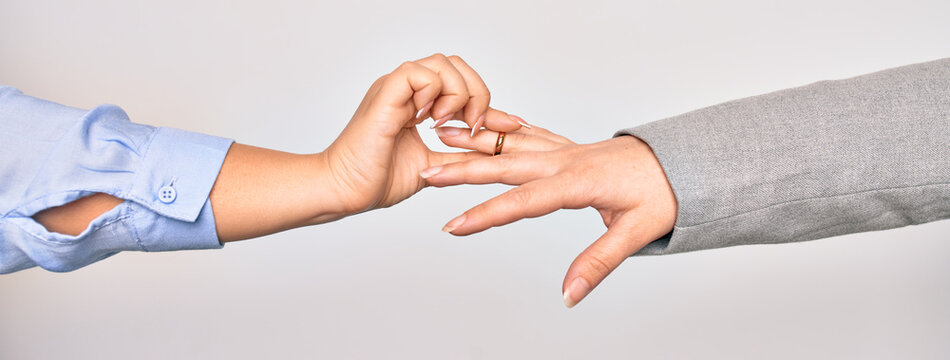 Hand of caucasian young woman putting golden marriage ring to other person over isolated white background