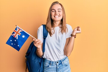 Beautiful blonde woman exchange student holding australia flag screaming proud, celebrating victory and success very excited with raised arm - obrazy, fototapety, plakaty