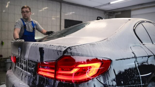 Man washing the car back after shampooing the bodywork wiping the car surface with a special cleaning glove.