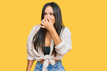 Young beautiful hispanic girl wearing casual clothes smelling something stinky and disgusting, intolerable smell, holding breath with fingers on nose. bad smell - obrazy, fototapety, plakaty
