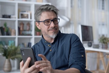 Happy white older man using phone, talking on video chat at home. Conference call with friend, family or work. Reading social media.