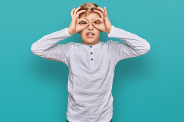 Little caucasian boy kid wearing casual clothes doing ok gesture like binoculars sticking tongue out, eyes looking through fingers. crazy expression.