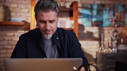 Fototapeta premium Portrait of happy mature man sitting at table using laptop at home working in home office.