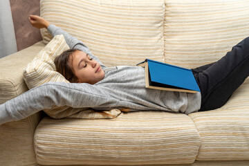 Cute little girl napping with a book she has just read on the sofa in her living room. Selective concept.