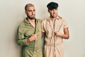 Homosexual gay couple standing together wearing casual jumpsuit pointing aside worried and nervous with forefinger, concerned and surprised expression