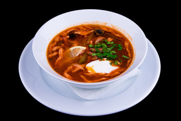 Traditional Russian soup Solyanka cooked with meat, sausages, salted cucumbers and olives sprinkled with herbs and seasoned with sour cream