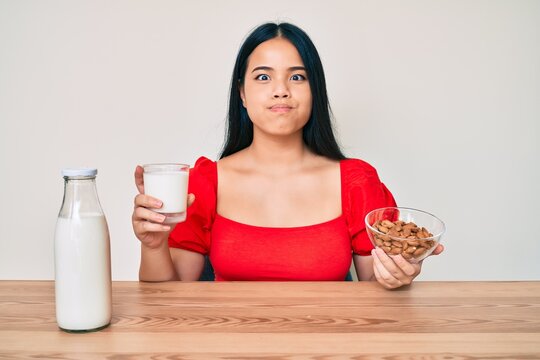 Young asian girl drinking healthy almond milk puffing cheeks with funny face. mouth inflated with air, catching air.