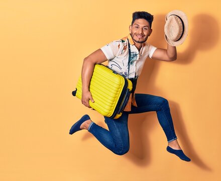 Young handsome latin man on vacation wearing summer clothes smiling happy. Jumping with smile on face holding cabin bag over isolated background