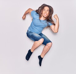 Young handsome man with long hair wearing casual clothes smiling happy. Jumping with smile on face celebrating with fists up over isolated white background.