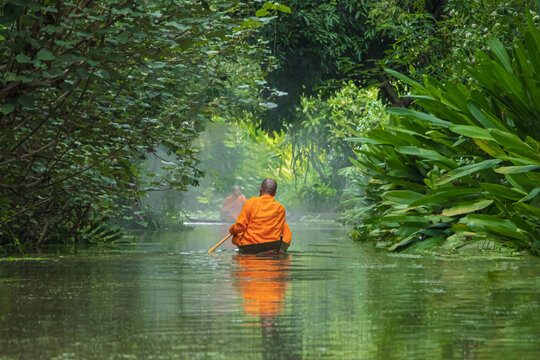 Monks rowing alms on the canal in the morning Through a tree tunnel In the water there is a reflection,The culture tradition Buddhist monk of making merit .