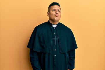 Obraz premium Young latin priest man standing over yellow background looking at the camera blowing a kiss on air being lovely and sexy. love expression.