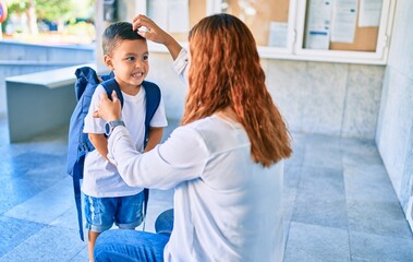 Adorable latin student boy and mom at school. Mother preparing kid putting up backpack.