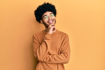 Fototapeta na wymiar Young african american man with afro hair wearing casual winter sweater looking confident at the camera with smile with crossed arms and hand raised on chin. thinking positive.