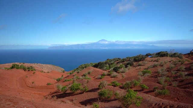 La Gomera - Rote Landschaft mit gr&uuml;nen B&uuml;schen im Norden nahe dem Mirador de Abrante mit Blick nach Teneriffa mit Teide