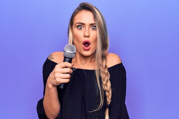Young beautiful blonde singer woman singing using microphone over purple background scared and...