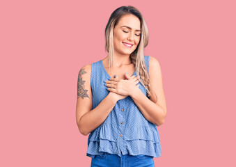 Young beautiful blonde woman wearing casual sleeveless t-shirt smiling with hands on chest with closed eyes and grateful gesture on face. health concept.