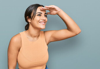 Fototapeta premium Young brunette woman wearing casual clothes very happy and smiling looking far away with hand over head. searching concept.