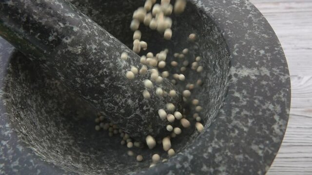 Close-up of the white peppercorns falling into the grey stone mortar in slow motion