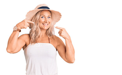 Obraz na płótnie Canvas Middle age fit blonde woman wearing summer hat smiling cheerful showing and pointing with fingers teeth and mouth. dental health concept.