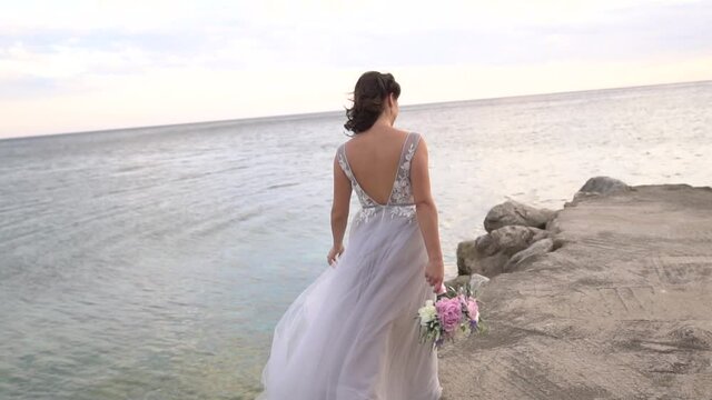 a bride with a wedding bouquet walks along the pier, her skirt fluttering in the wind